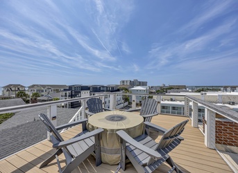Rooftop terrace with sweeping coastal views, comfortable Adirondack seating, and a covered fire pit on warm wood decking. Perfect for morning coffee or evening relaxation with sea breezes and ocean views.