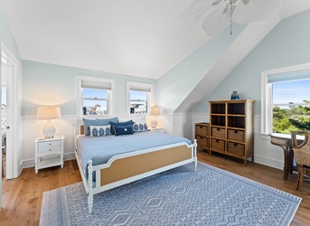 Sink into soft coastal calm in your bedroom, where vaulted ceilings and soft blue tones create a breezy retreat. Wake to glimpses of lush greenery and salty air through generous windows that frame your peaceful escape.
