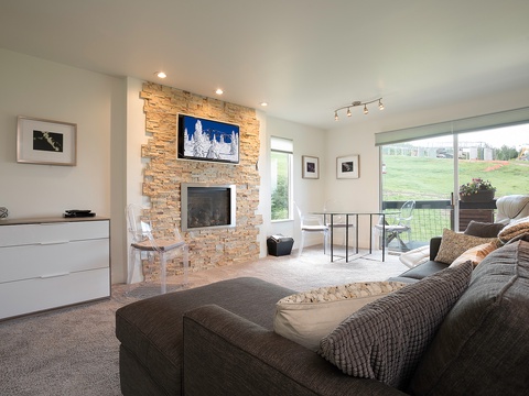 Unwind in your spacious living room featuring a cozy stone fireplace, large windows framing the golf course, and plush seating perfect for relaxing evenings.
