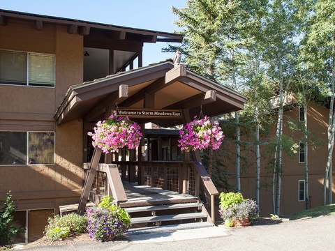 The welcoming entrance to Storm Meadows East, framed by vibrant hanging flower baskets and surrounded by mature trees, marks the arrival point to the property.