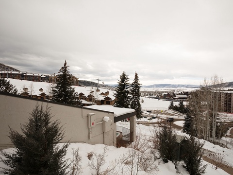 A winter scene showcasing snow-covered rooftops and evergreens nestled against a mountain backdrop, capturing the property's serene alpine setting and nearby ski area access.