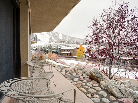 This expansive balcony frames stunning mountain views, with ski slopes visible in the distance. The outdoor seating area offers an ideal spot for enjoying crisp alpine air year-round.