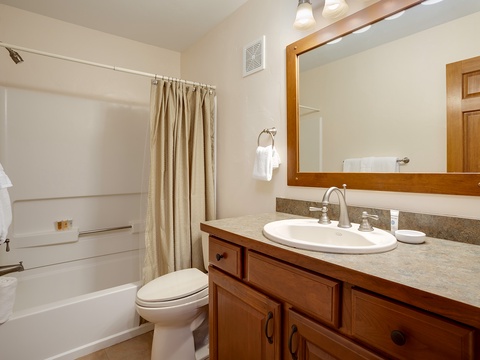 Your private bathroom features a tub-shower combo, warm wood vanity with granite countertop, and fresh towels ready for your stay.