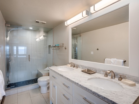 Step into your modern bathroom with dual sinks, marble counters, and a sleek glass-enclosed shower. Fresh towels await your arrival.