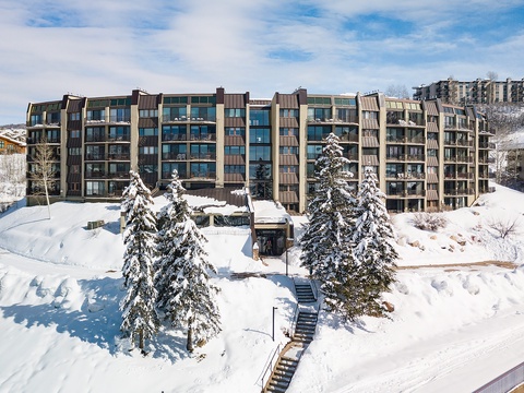 A modern mountain property set in a pristine winter landscape with snow-dusted evergreens and ski-in access, surrounded by neighboring resorts and hillside vistas.