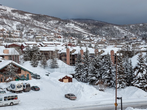 Snow-blanketed mountain village with ski slopes rising beyond, nestled among evergreens beneath overcast winter skies—a classic alpine destination surrounded by winter recreation terrain.