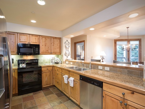 This bright, fully-equipped kitchen invites you to prepare meals with modern appliances, granite countertops, and warm wood cabinetry. Natural light streams through large windows overlooking scenic mountain views.