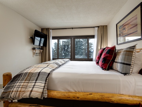 Wake up to snowy pines framed by your bedroom window, cozy plaid bedding inviting you to rest, and a rustic log bed bringing mountain charm to your stay.