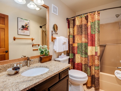 Step into your beautifully appointed bathroom with warm wood accents, granite counters, and plush towels awaiting your arrival. The charming autumn-themed shower curtain adds a cozy, inviting touch to your private retreat.