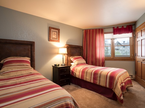 Cozy twin bedroom with warm striped linens, bedside reading lamps, and mountain views through your window—perfect for restful nights after a day of adventure.