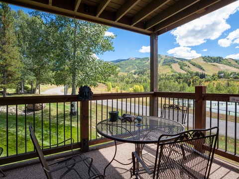 This property features a covered terrace with mountain views, perfect for enjoying the scenic alpine landscape. The outdoor setting includes dining furniture and faces rolling hills with ski slopes and lush greenery.