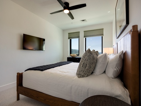 Drift off in your serene bedroom where modern comfort meets mountain tranquility. Natural light fills the space through large windows, revealing rolling hills that frame your peaceful retreat.