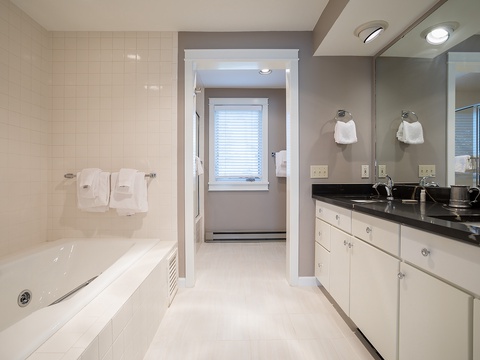 Your private spa-like bathroom features a soaking tub, dual vanities with granite counters, fresh towels, and bright recessed lighting for a serene, luxurious retreat.