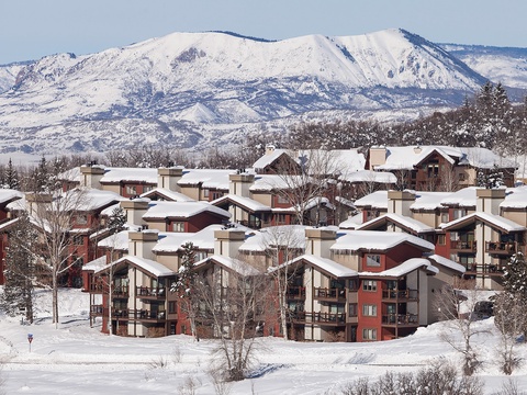 A mountain resort complex nestled among snow-covered peaks and forested slopes, offering convenient access to winter recreational activities in a scenic alpine setting.