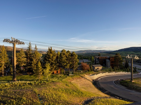 Property located in a scenic mountain valley setting, accessed via a curving residential road surrounded by evergreen trees and open hillside terrain.