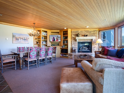 Settle into your cozy mountain retreat with a crackling fireplace, comfortable seating, and mountain views through expansive windows—perfect for gathering after a day of adventure.