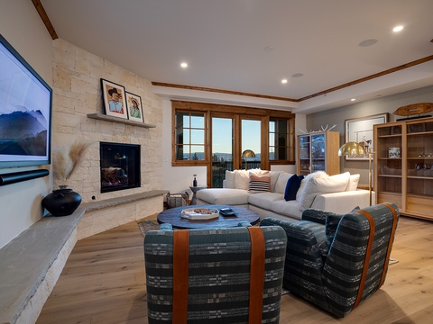 Curl up in your spacious living room with plush seating around the fireplace, where modern comfort meets rustic charm. Enjoy movie nights on the big screen or watch stunning views unfold through expansive windows.