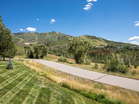A peaceful residential area nestled at the base of rolling, tree-covered mountains with clear blue skies overhead, offering natural beauty and quiet surroundings for guests seeking a mountain retreat.