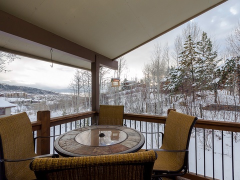 A covered deck frames snow-dusted evergreens and distant mountain ridges, providing a sheltered outdoor setting at the property's perimeter during the winter season.