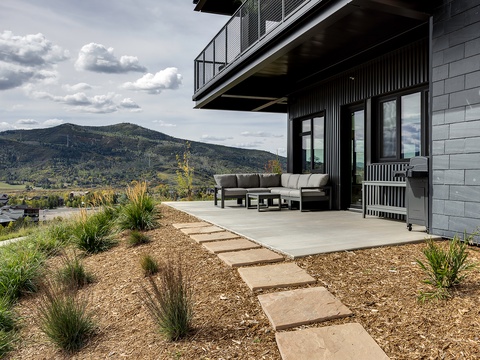 The property features a modern terrace with contemporary outdoor furniture and mountain views, set amid a thoughtfully landscaped garden with native grasses and stepping stones.