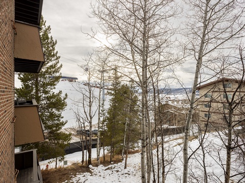 Winter setting with snow-covered landscape, mountain views, and brick buildings nestled among evergreen and bare deciduous trees.