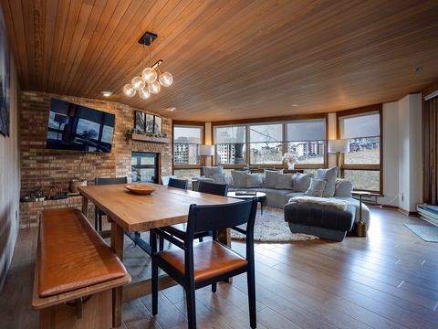 Gather around the warm wooden table or sink into the plush sectional sofa in this inviting open-concept space. Natural light floods through expansive windows, highlighting the cozy fireplace and stylish décor perfect for your mountain getaway.