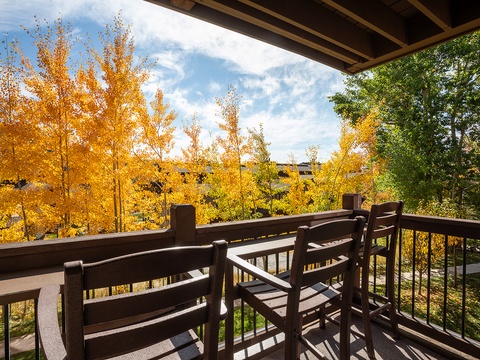A balcony with seating that overlooks brilliant autumn foliage in golden yellow and green tones against a bright blue sky.