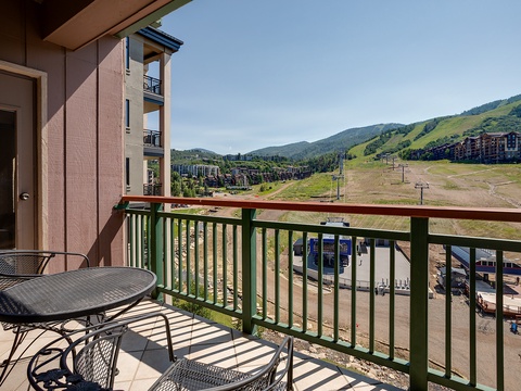 A mountain resort setting with ski runs and surrounding peaks, adjacent to the building's vacation rental units. Base area visible below with seasonal ski infrastructure and green mountain slopes.
