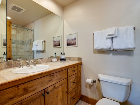 Step into your beautifully appointed bathroom, where warm wood cabinetry and stone countertops create a welcoming retreat. Fresh towels await, and a spacious walk-in shower promises a refreshing start to each day.