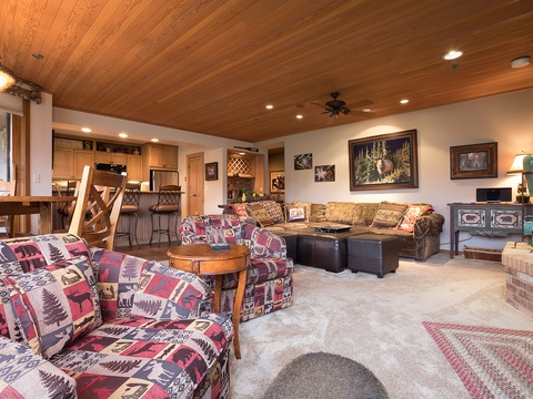 Sink into rustic comfort in your open-concept living space, where wood-paneled ceilings, cozy sofas, and warm lighting create a welcoming mountain retreat perfect for gathering after a day of adventure.