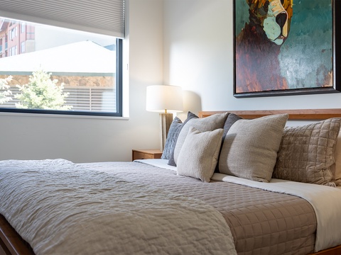 Sink into this inviting bed dressed in soft linens and stacked pillows. Natural light spills through your window, while thoughtful art adds character to your peaceful retreat.