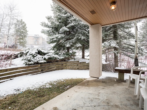 Covered patio with seating overlooks a peaceful winter landscape with snow-dusted evergreens and a private, fenced yard—a quiet spot to enjoy all seasons.