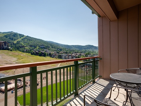 Balcony overlooks a mountain resort community surrounded by forested slopes and rolling terrain, offering views of nearby properties and the valley below.