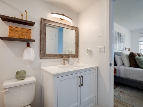 A bright, thoughtfully designed bathroom connects to your bedroom, featuring a modern vanity, open shelving with coastal touches, and crisp white finishes for a clean, relaxing feel.