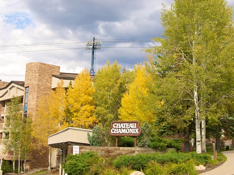 Chateau Chamonix property entrance surrounded by vibrant autumn aspens and evergreens, set against dramatic mountain skies and residential buildings.