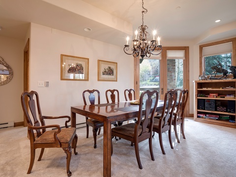 Gather around this elegant dining table for memorable meals together. The chandelier overhead sets a warm ambiance, while natural light streams in through large windows overlooking the trees.