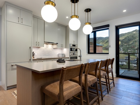 Your modern kitchen glows with natural light, where a spacious island with seating invites casual meals while you take in stunning mountain vistas through large glass doors.