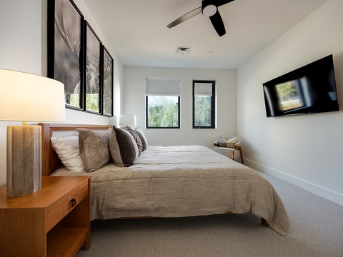 Drift off in your tranquil bedroom, where soft natural light filters through windows and a gentle ceiling fan keeps you comfortable. The minimalist design and plush bedding create a restful retreat after exploring the area.