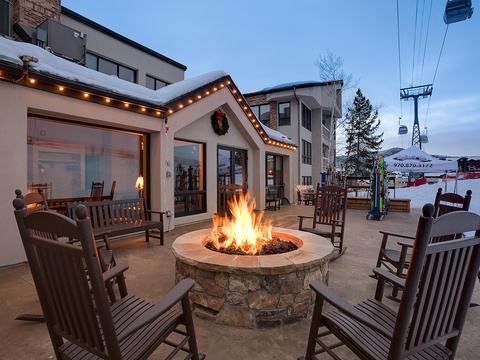 The property features a cozy stone fire pit surrounded by wooden rocking chairs on a spacious patio, offering a charming gathering spot near ski lifts and mountain slopes.