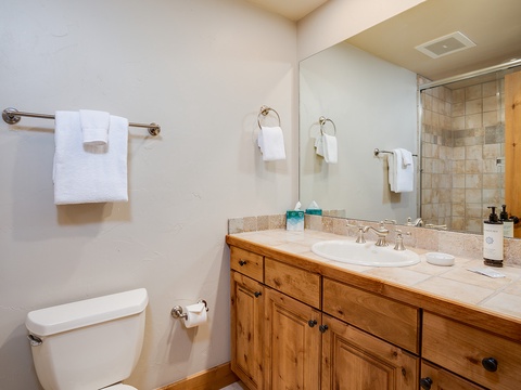 Freshen up in your private bathroom featuring a stone vanity with rustic wooden cabinetry, fluffy towels, and a spacious walk-in shower—everything you need for a refreshing start to your day.