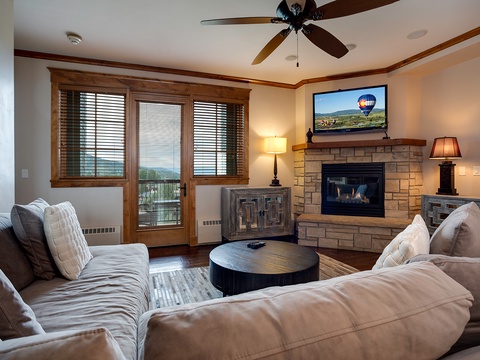 Unwind in your spacious living room with a crackling stone fireplace, plush seating, and serene mountain views through the balcony doors—your perfect retreat after adventure.