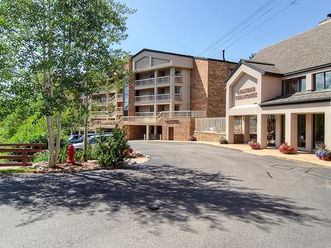 The property entrance features a multi-story lodge-style building with convenient parking and landscaped surroundings, located in a peaceful mountain setting with nearby trees and scenic views.