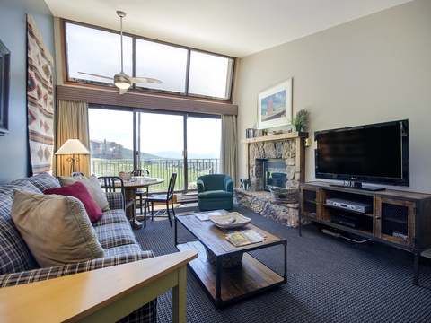 Relax in your cozy living room with mountain views, a crackling stone fireplace, and comfortable seating—perfect for unwinding after a day of adventure.