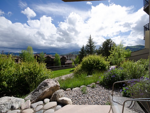 A landscaped garden terrace offering serene mountain views and lush greenery. The property sits in a peaceful area surrounded by trees, natural rock features, and neighboring buildings nestled in a scenic valley.