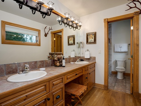 Your private bathroom features a double vanity with ample counter space, rustic wood cabinetry, and charming décor that blends mountain elegance with modern comfort.