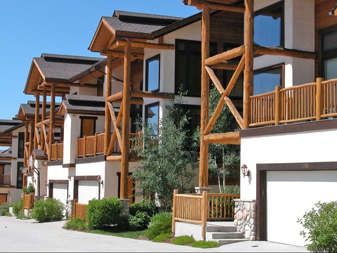 Charming alpine-style property featuring warm timber balconies and white stone accents set against a clear blue sky.