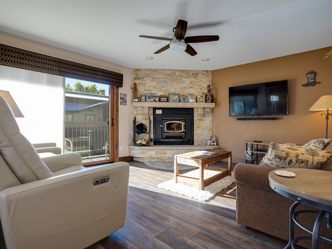 Unwind in your spacious living room, where a stone fireplace adds warmth, plush seating invites relaxation, and natural light streams through sliding doors to the balcony.