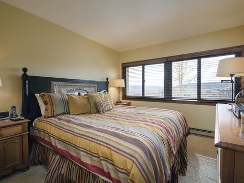 Sink into this inviting bed dressed in warm stripes and plush pillows. Soft lamps flank your nightstand, while wide windows frame a peaceful view to start your day.