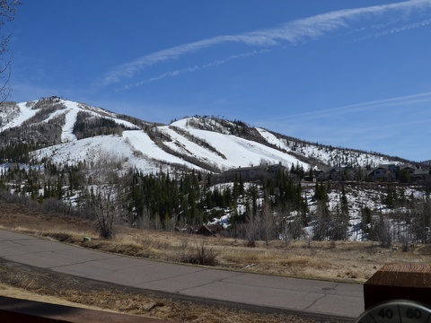 Snow-covered mountain slopes framed by evergreen trees create a stunning alpine setting, visible from the property's surrounding neighborhood during late winter or early spring.