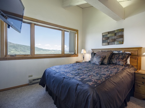 Wake up to stunning mountain vistas framed by large windows. Your cozy bedroom features plush bedding, warm wood furnishings, and peaceful views that make every morning special.